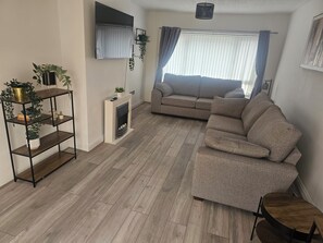 Ein Wohnzimmer mit einer Couch, einem an der Wand befestigten Fernseher, einem Kamin und einem Holzboden.
