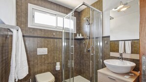 Een badkamer met een douche met glazen wand, een wit wastafel, een toilet en een spiegel boven het wastafel.