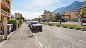 A street with parked cars, a building with balconies, and mountains in the background.