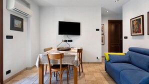 A dining area with a table, chairs, a flat-screen TV, and a blue sofa.