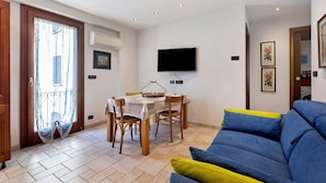 A living room with a blue sofa, a dining table with chairs, a TV mounted on the wall, and a door with a curtain.