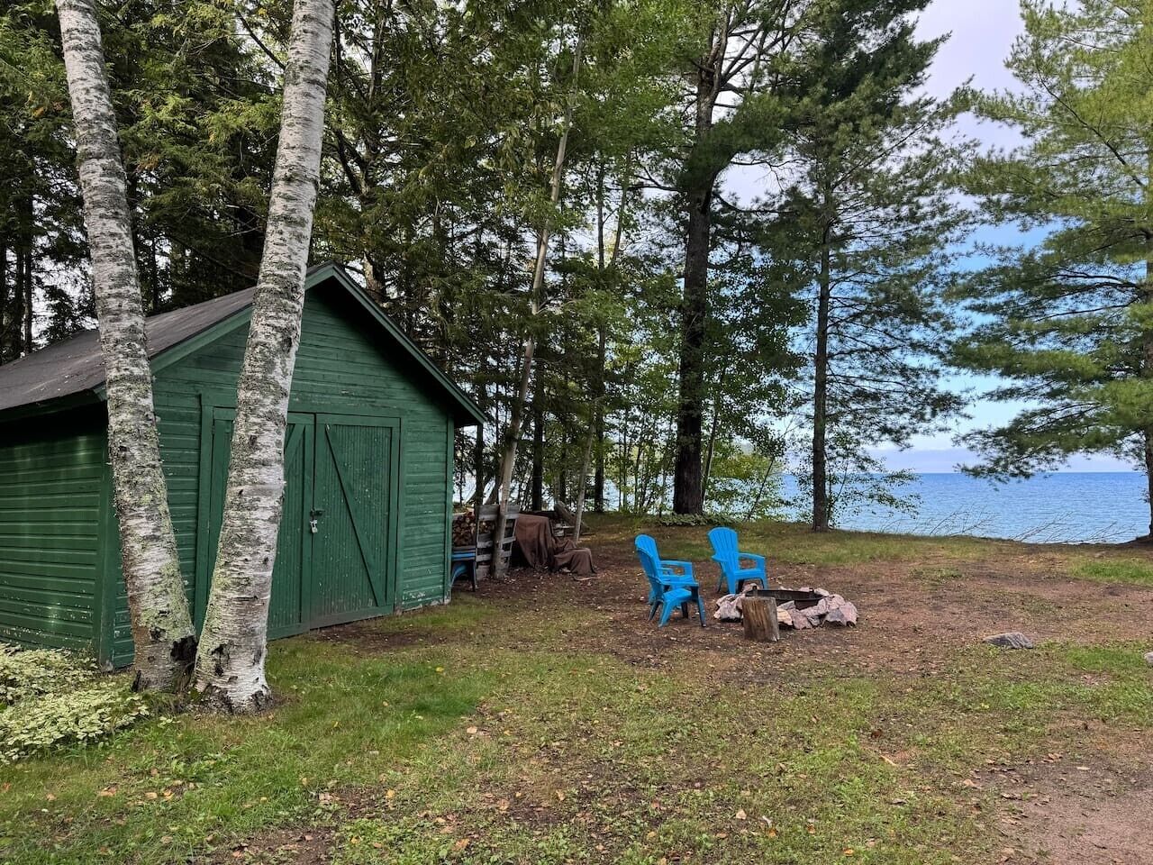 Un abri de jardin vert, deux chaises bleues, un foyer et une vue sur le lac.