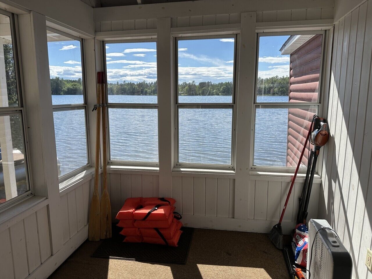 A room with a view of a lake, wooden paddles, a life jacket, and a broom.