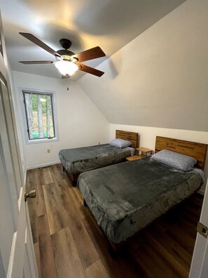 Ein Schlafzimmer mit zwei Betten, einem Deckenventilator, einem Fenster und Holzboden.
