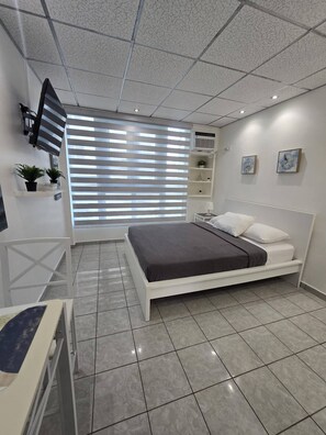 Un dormitorio moderno con una cama, un escritorio, una silla, un televisor y una ventana con persianas.