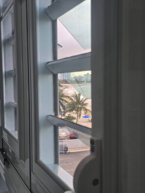 A window with a view of a beach, palm trees, and a parking area. - LIS4B12 - SeaSide Beach II (Carolina)