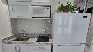 Ett modernt kök med vita skåp, en inbyggd mikrovågsugn, ett kylskåp och en diskho med en bänkskiva i granit.