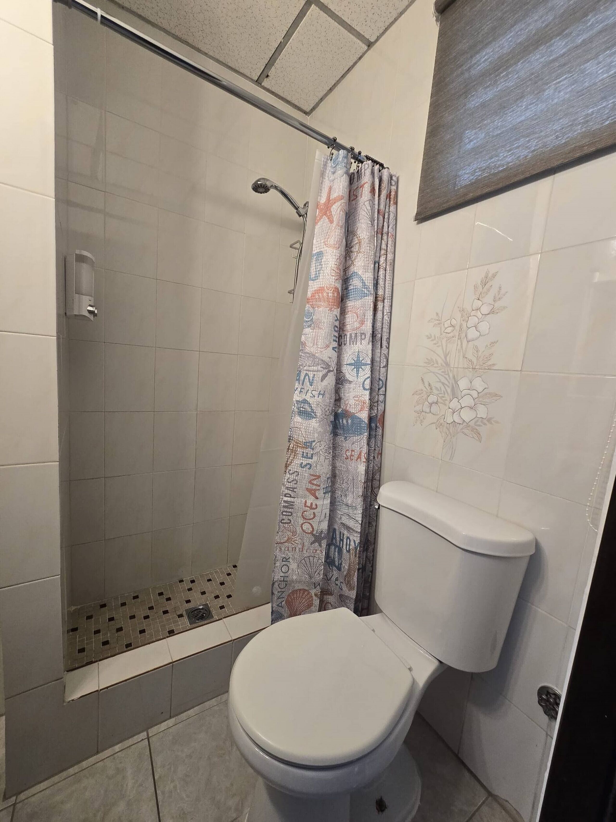A bathroom with a toilet, a shower with a glass door, and a curtain with nautical patterns.