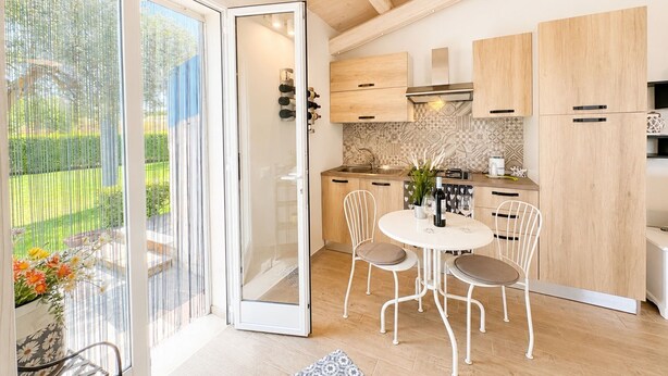 Een moderne keuken met houten kastjes, een eethoek met witte stoelen, en een schuifdeur naar een tuin.