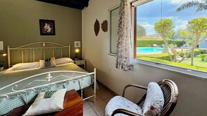 Een slaapkamer met een bed, een stoel, een raam met uitzicht op een zwembad en tuin.