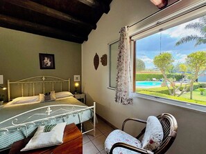 Ein Schlafzimmer mit Bett, einem Sessel, einem Fenster mit Blick auf Pool und Garten.