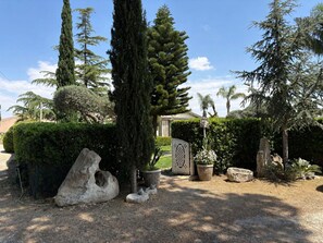 Ein angelegter Garten mit verschiedenen Bäumen, einer großen Felsenformation und einem Tor.