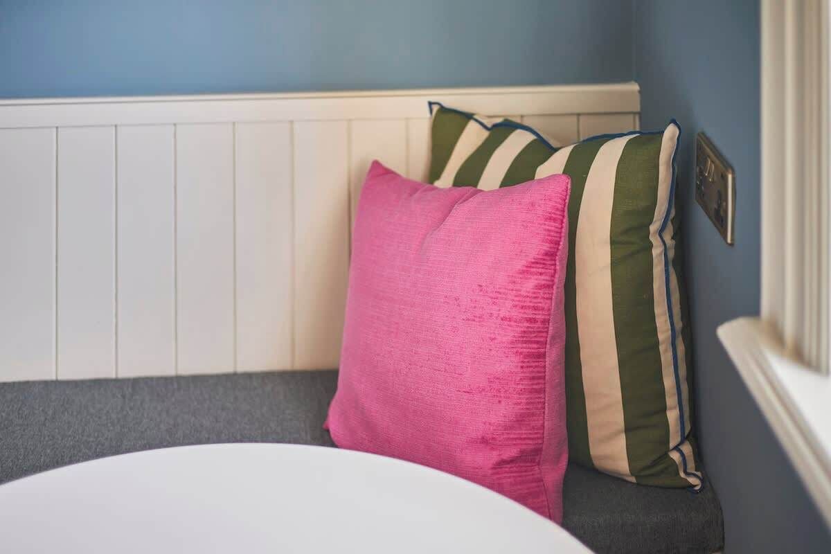 Una habitación con cabecera blanca, sofá gris y almohada rosa.