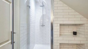 A bathroom with white subway tiles, a glass shower enclosure, and a black object on a shelf.