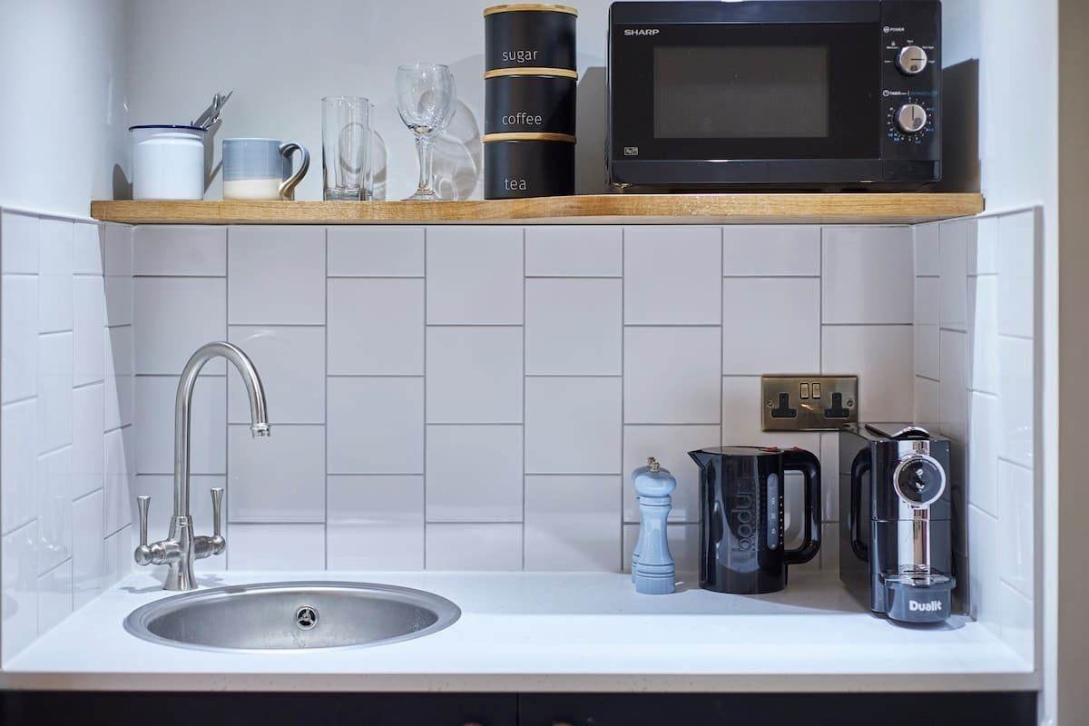 A kitchen with a sink, a microwave, a coffee maker, and a kettle on the countertop.