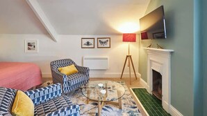 A room with a bed, two patterned sofas, a glass coffee table, a floor lamp, a fireplace, and wall-mounted artwork.