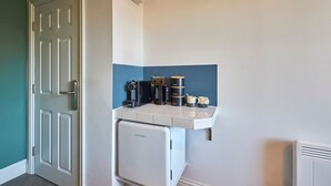 A compact kitchenette with a coffee maker, tea and coffee containers, a mug, and a mini fridge.
