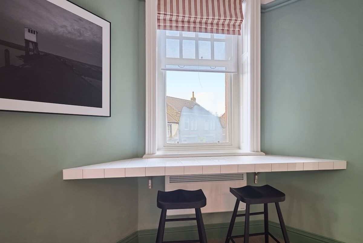 A corner room with a bay window, a radiator, and two black stools.