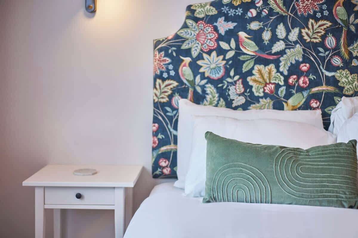 Ein Bett mit einem blumigen Kopfstück, ein weißer Nachttisch mit einer Schublade und ein grünes Kopfkissen.