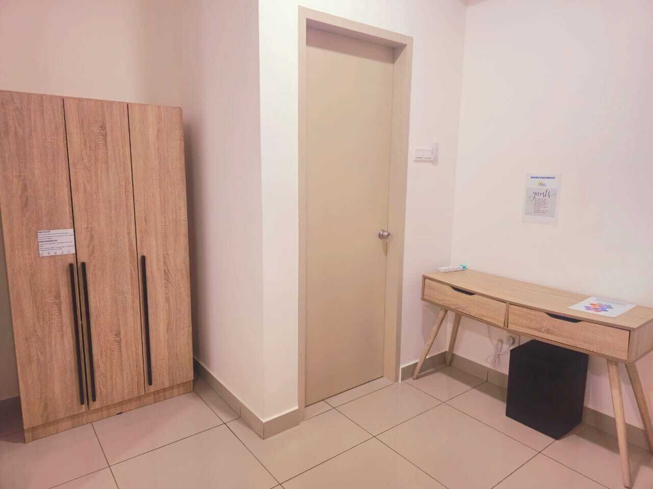 A room with a wooden wardrobe, a door, a desk with drawers, and a small black speaker.