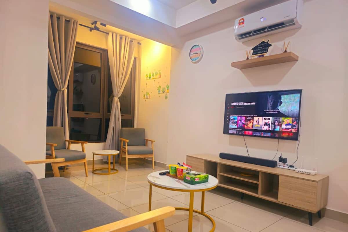 Ein Wohnzimmer mit Fernseher, Sofa, Sesseln, einem kleinen Tisch und einer Wandregal.