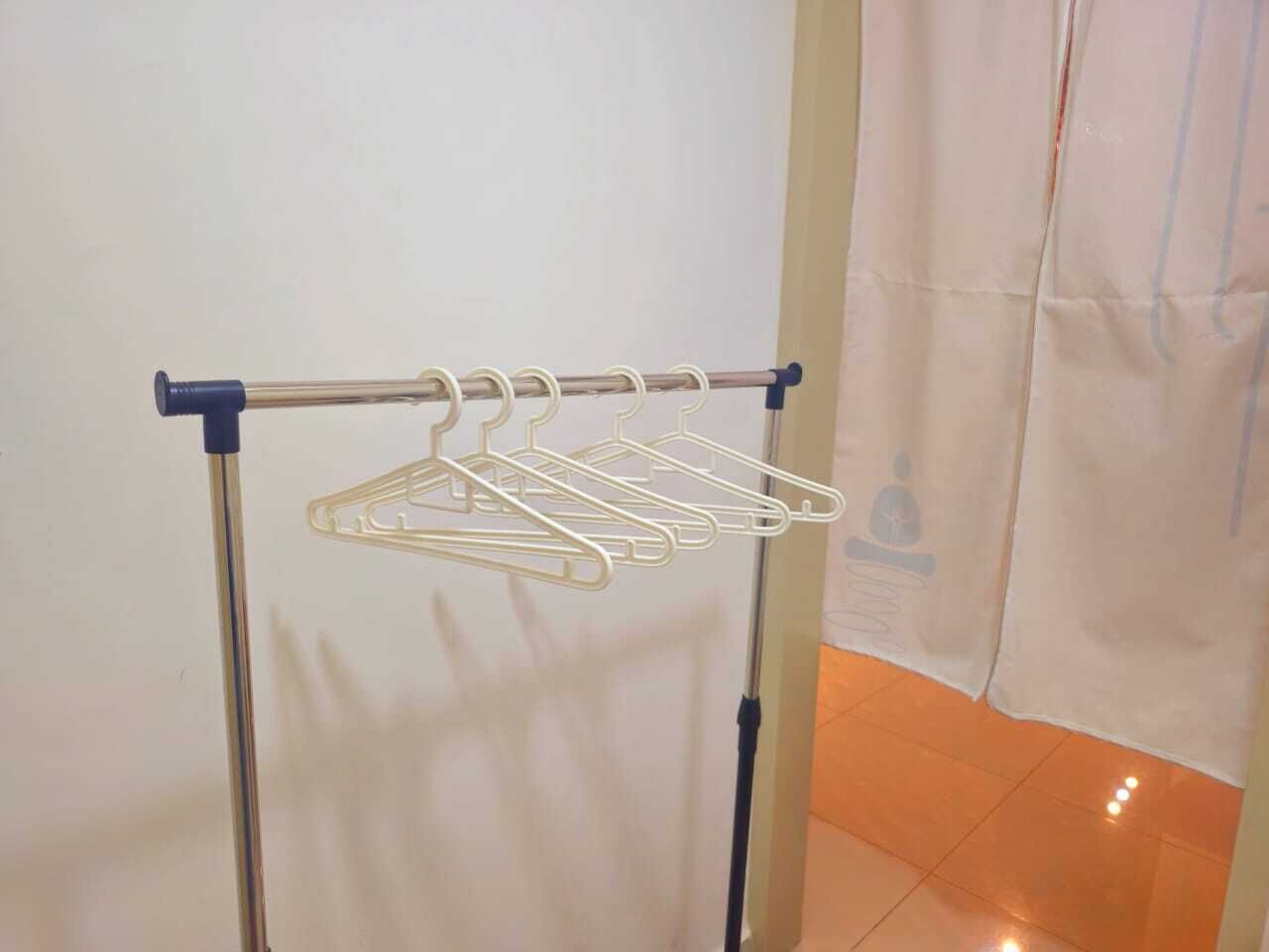 A metal drying rack with multiple white hangers against a white wall.