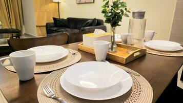 A dining table set with plates, cups, and cutlery, with a vase and a lamp in the background.