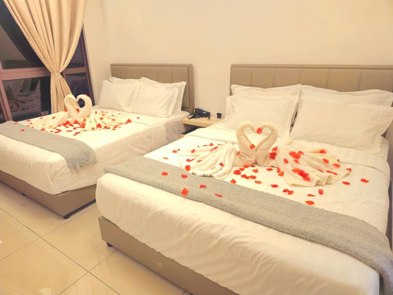 Two beds with white linens, heart-shaped towels, and rose petals.