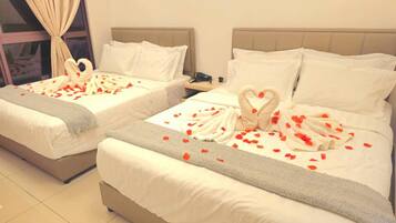 Two beds with white linens, heart-shaped towels, and rose petals.