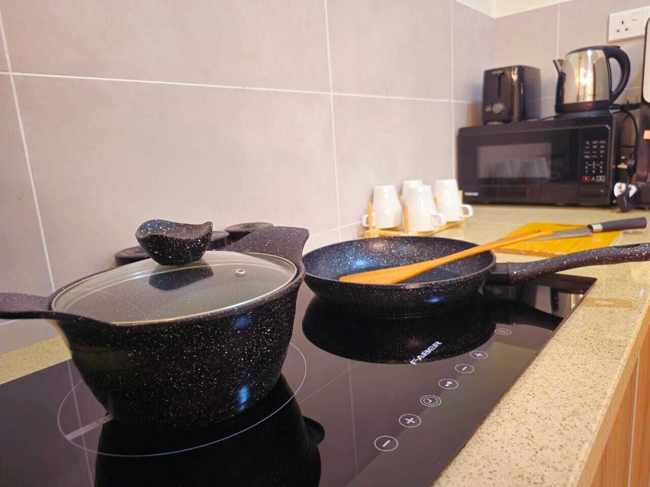 A kitchen with a stove, two pots, a frying pan, and a coffee maker.
