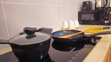 A kitchen with a stove, two pots, a frying pan, and a coffee maker.