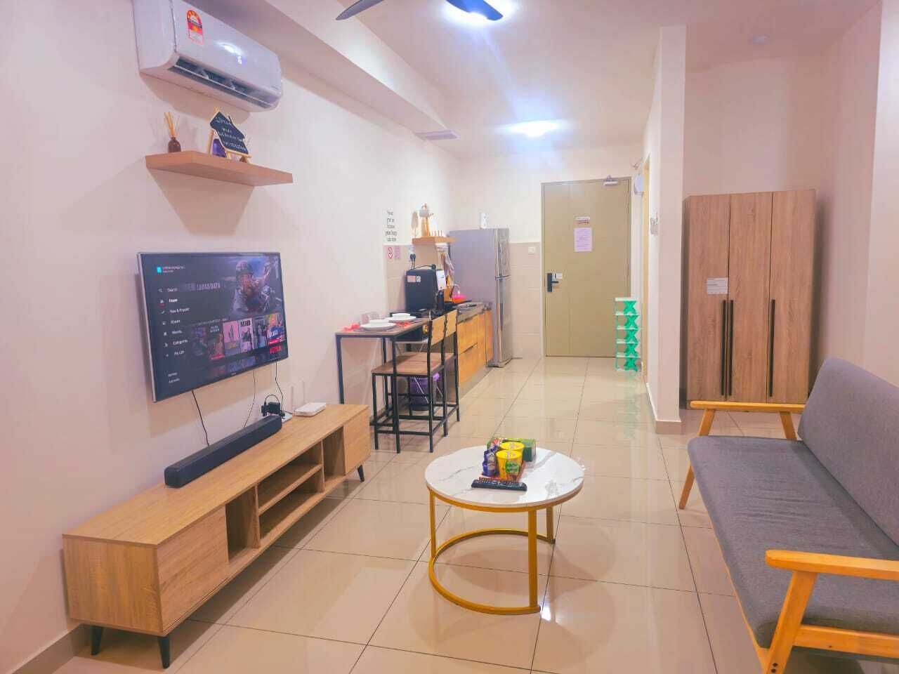 A living room with a TV, a sofa, a coffee table, a desk with a chair, and a kitchen area in the background.