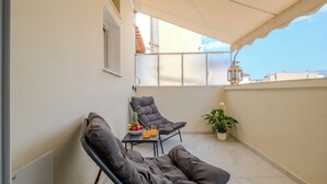 Ein Balkon mit zwei Liegestühlen, einem kleinen Tisch mit Obst und Getränken, einem Blumentopf und Blick auf die Stadtlandschaft.