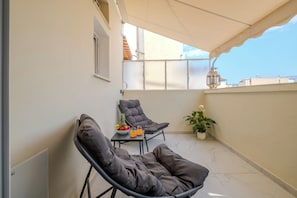 Ein Balkon mit zwei Liegestühlen, einem kleinen Tisch mit Obst und Getränken, einem Blumentopf und Blick auf die Stadtlandschaft.