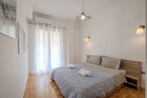 Ein Schlafzimmer mit einem Bett, einem Holzkopfende, einer Pendelleuchte und einem Fenster mit Vorhängen.