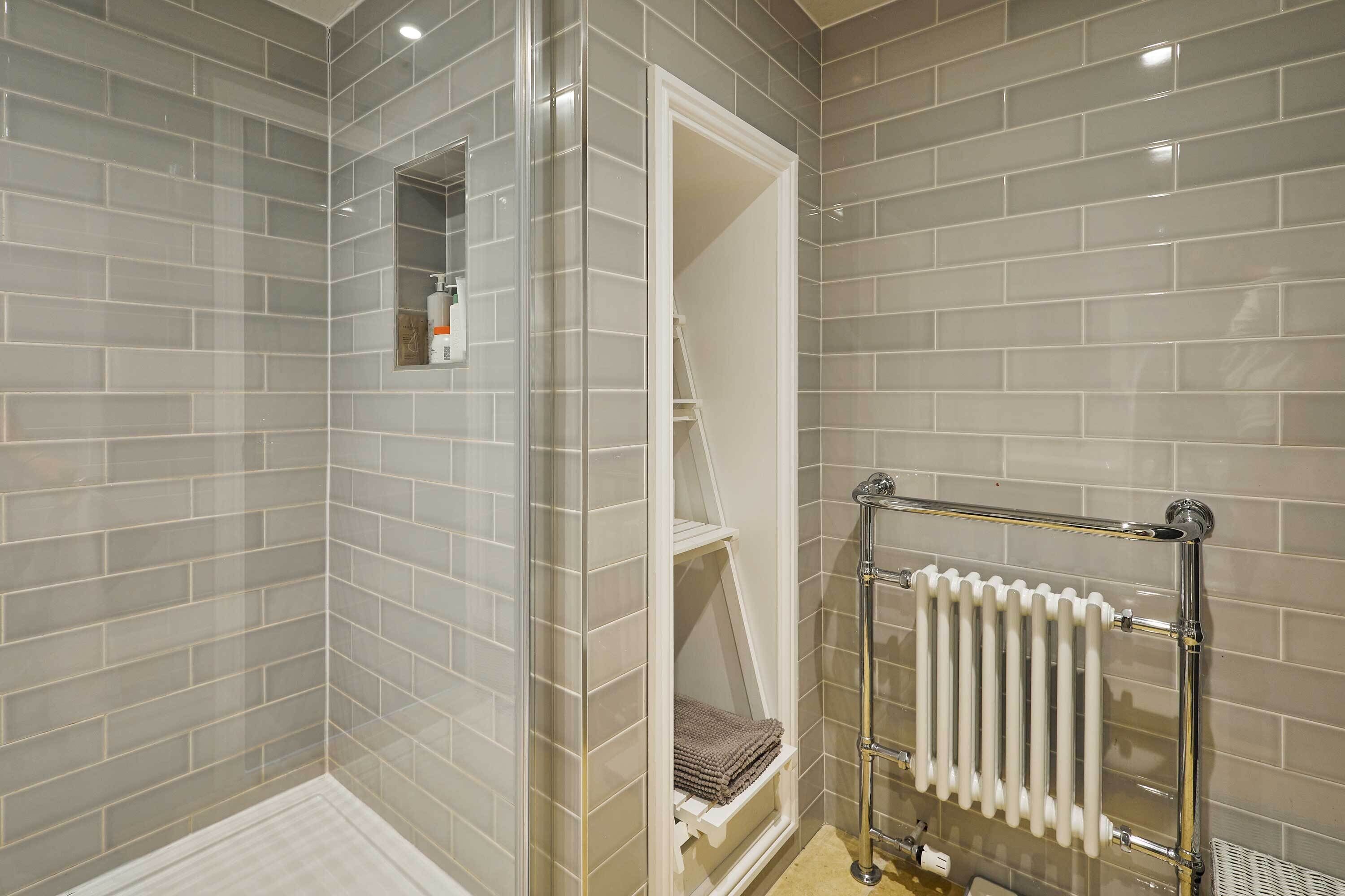 A bathroom with grey tiled walls, a white radiator, and a glass shower enclosure.