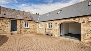 A stone building with a paved courtyard, a bench, and a covered entrance.