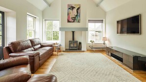 A living room with a brown leather sofa, a fireplace, a painting, and a TV mounted on the wall.
