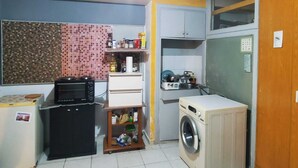 Een compacte keuken met een magnetron, een kleine koelkast, een wasmachine en een betegelde achterwand.