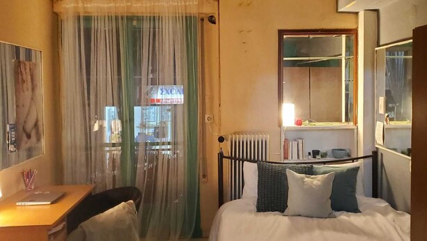 Een slaapkamer met een bed, een bureau, een stoel, een radiator en een raam met gordijnen.