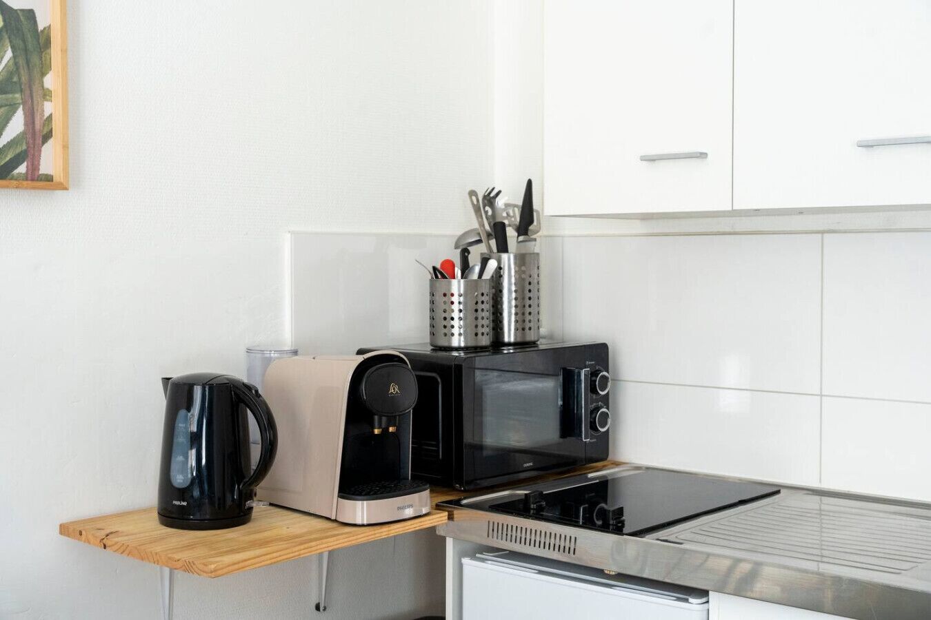 A kitchenette with a coffee maker, toaster, and microwave on a wooden shelf, and a stove on the countertop.