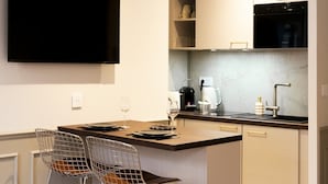 A modern kitchen with a flat-screen TV, a coffee maker, a kettle, and two bar stools. - Trendy studio apartment, 2 minutes from the very center of town (Caen)