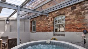 Ein Außenbereich mit Whirlpool, einer Ziegelwand, einer Pergola und einem Fenster.