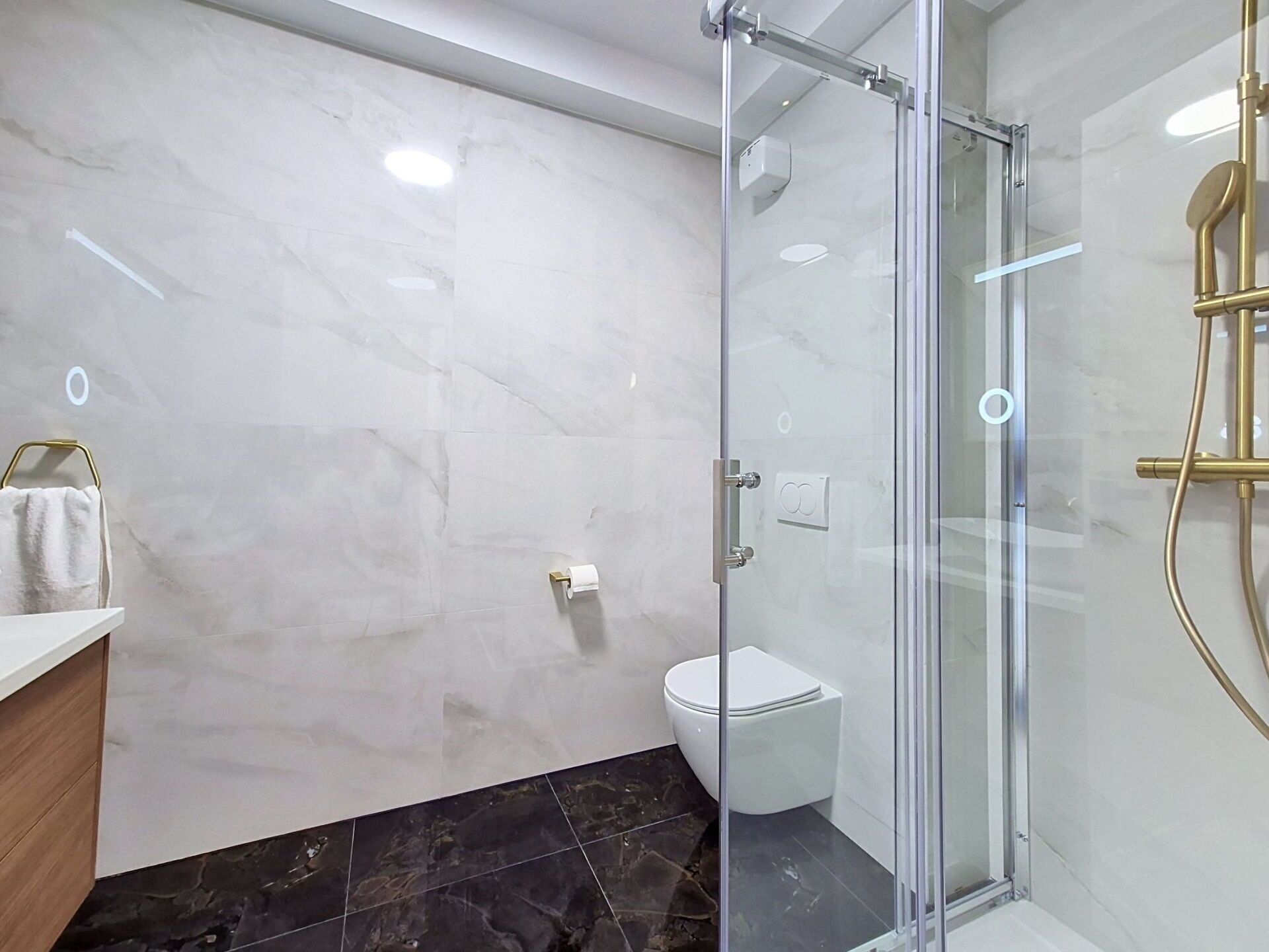 Um banheiro moderno com box de vidro, vaso sanitário branco e piso de mármore.