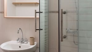 A bathroom with a glass-enclosed shower, a white sink, and a mirror with shelves. - Studio with free, private parking (Caen)