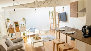 A modern living room with a sofa, a dining table with stools, a TV mounted on the wall, and a bookshelf with plants. - Studio with free, private parking (Caen)