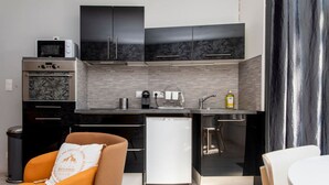 Een compacte keuken met een magnetron, oven en koelkast, een spoelbak en een klein eethoekje met een stoel en tafel.