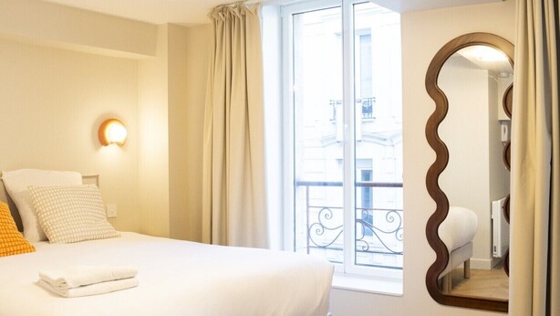 Habitación de hotel con cama, un ventanal grande, un espejo y vistas al exterior.