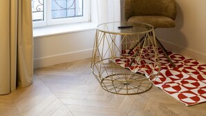 Una habitación con ventana, una mesa redonda, una silla, una lámpara de pared y una alfombra estampada.