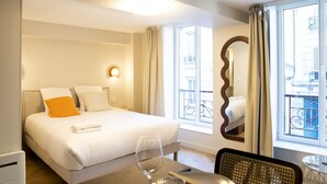 Habitación de hotel con cama, mesa de comedor con una silla, un espejo y ventana con cortinas.